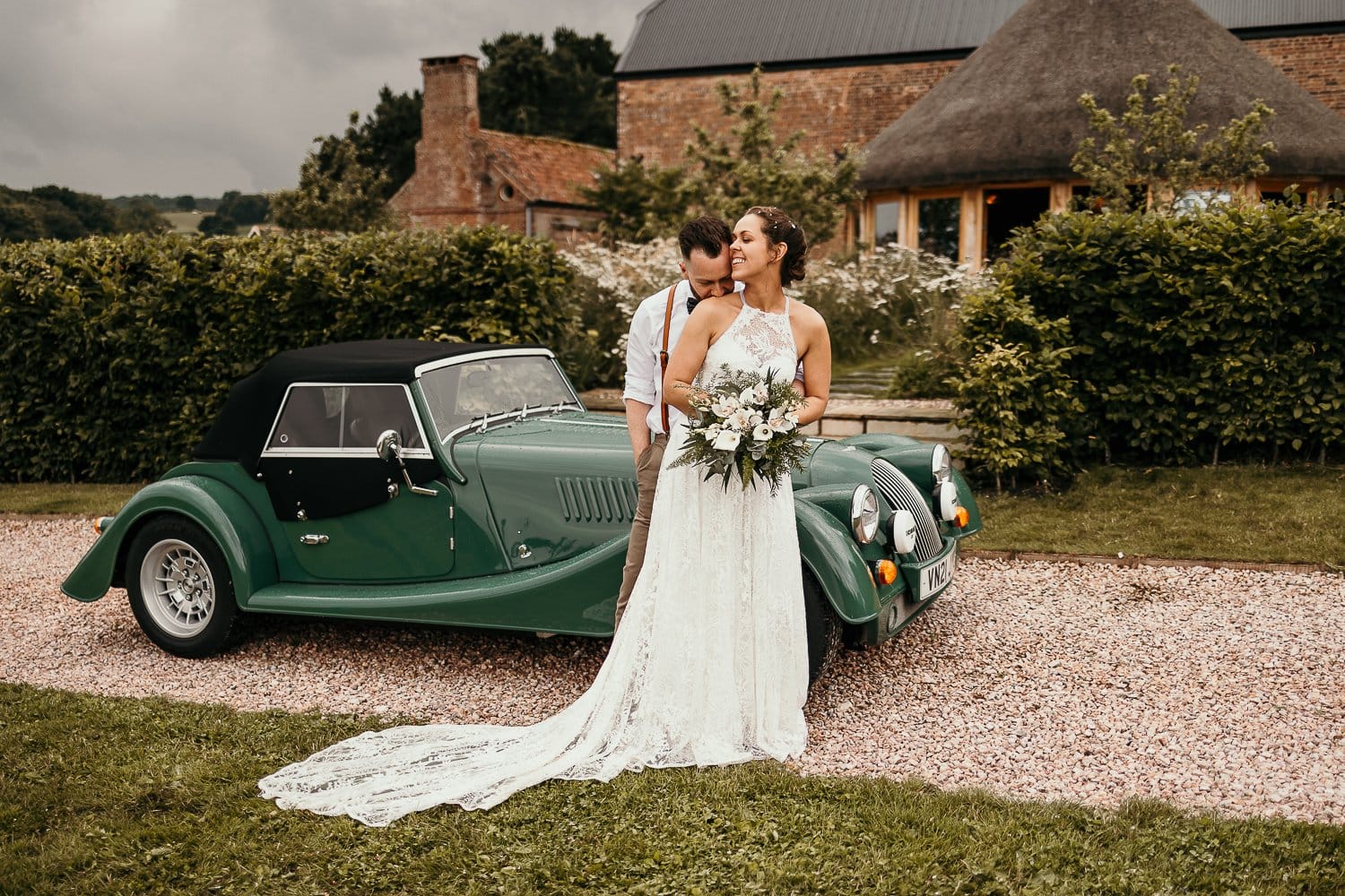 Bride and groom leaning on their morgan car